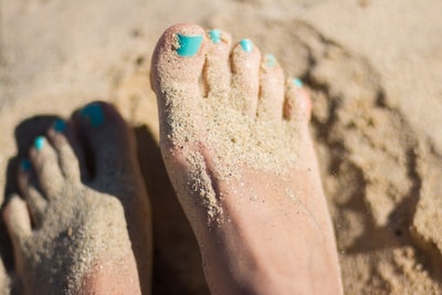 人天蓝色的指甲油的脚棕色的沙滩上

